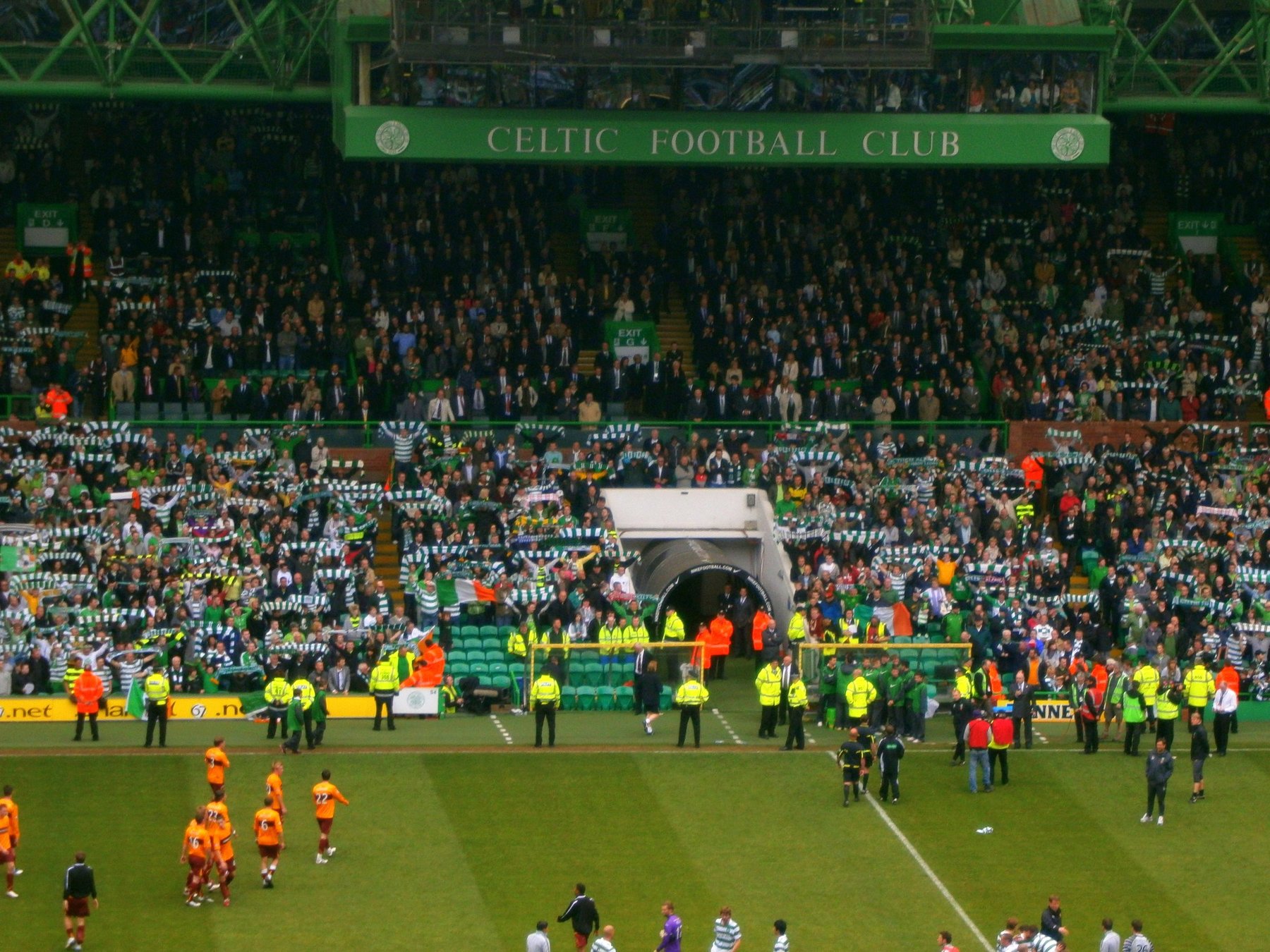 A packed stand at Celtic Park with stewards lining the trackside